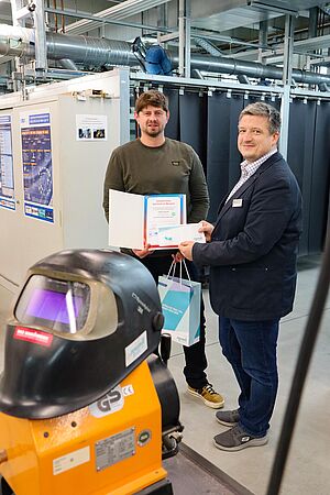 Martin Schmeider übergibt Steffen Nagorka sein Zertifikat. Im Hintegrund sind Schweißkabienen zu sehen.