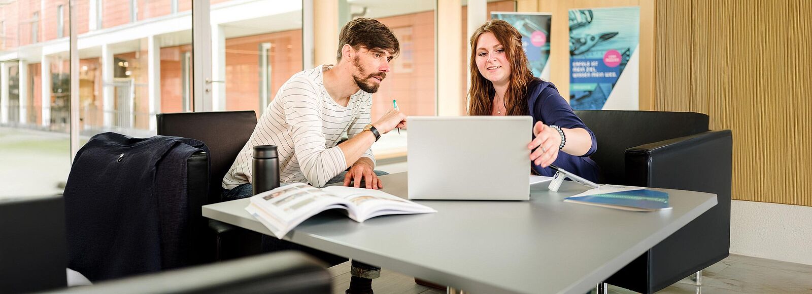 Zwei Personen sitzen beratend an einem Laptop im Foyer des njumii-Gebäudes.