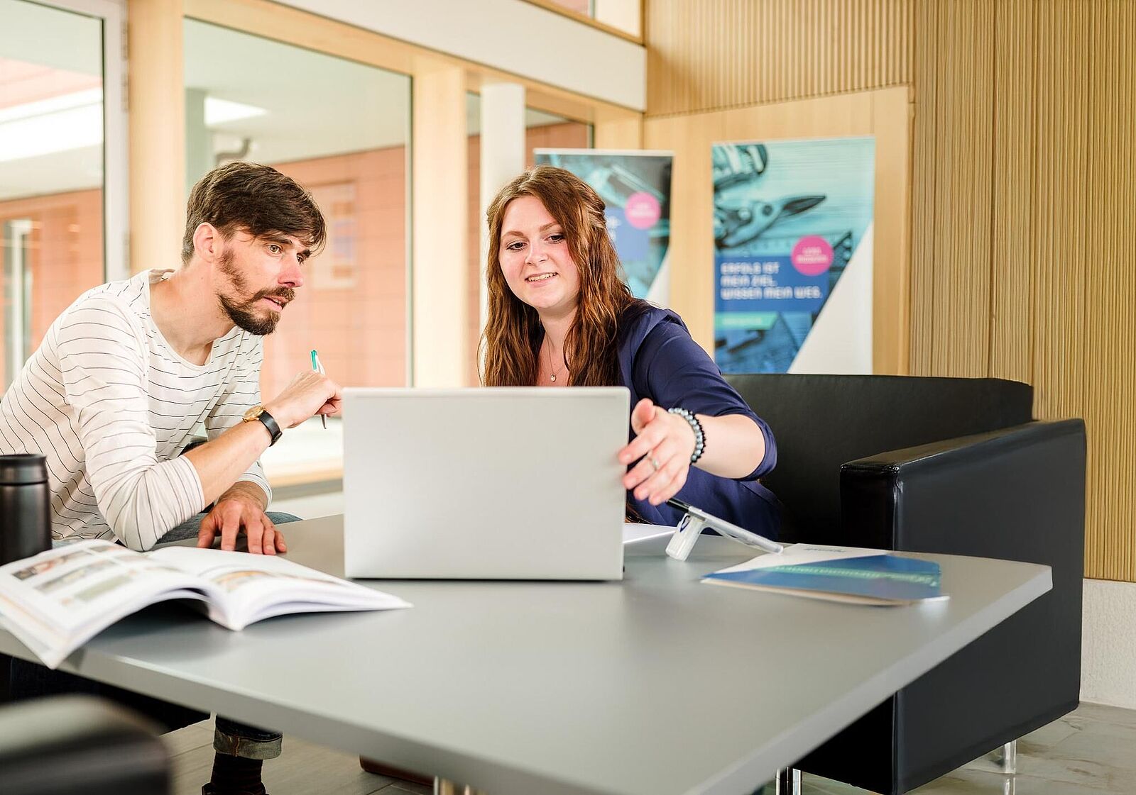 Zwei Personen sitzen beratend an einem Laptop im Foyer des njumii-Gebäudes.