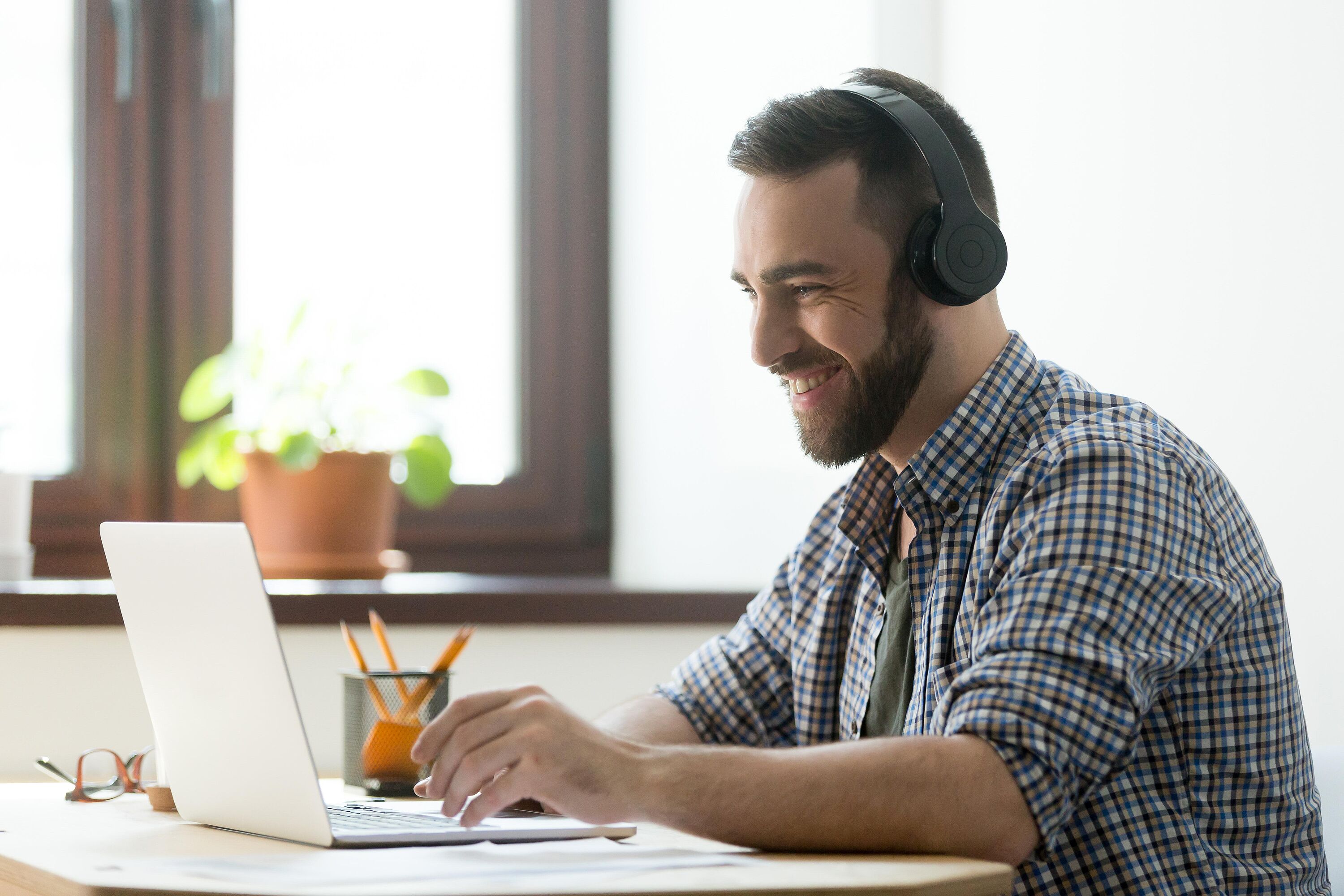 Eine Person sitzt mit Kopfhörern am Schreibtisch vor einem Laptop und verfolgt aktiv ein Webinar.