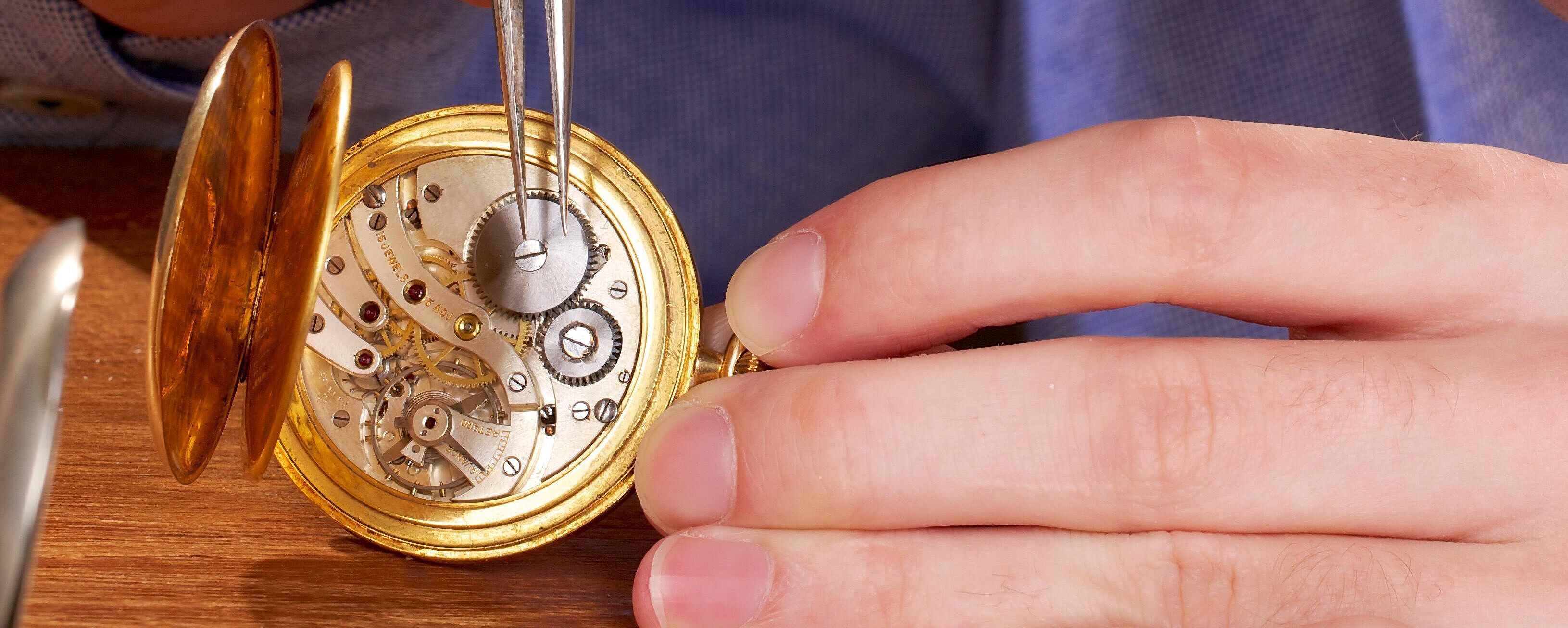 Ein Uhrmacher nimmt an einer geöffneten Uhr Reparaturarbeiten am Uhrwerk vor.
