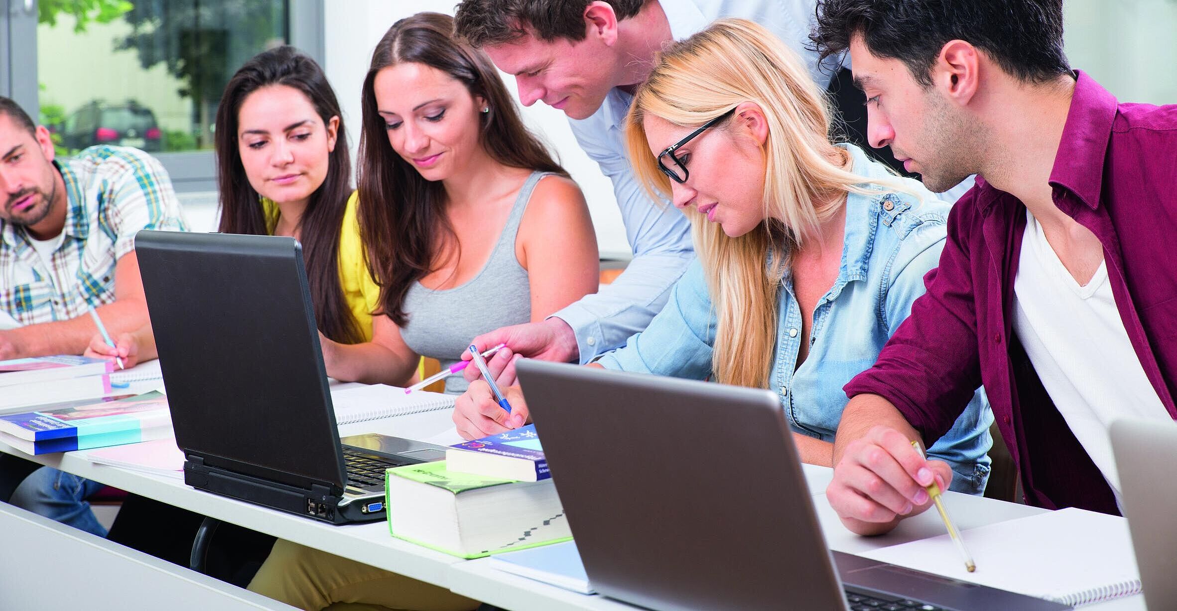 Mehrere Personen sitzen mit Laptops an einem Schreibtisch und bearbeiten gemeinsam Dokumente.