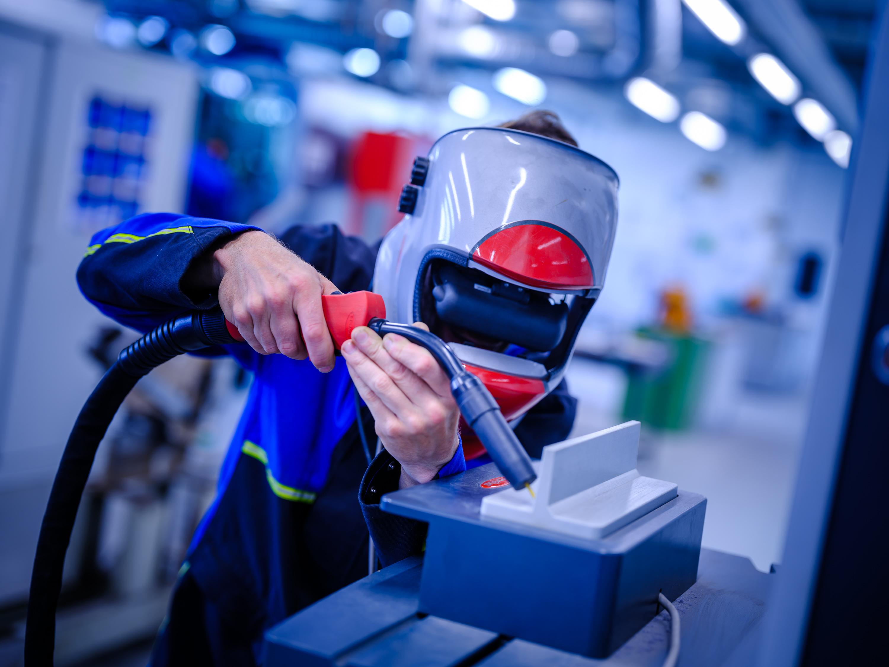 Eine Person in der Schutzkleidung eines Schweißers bei der Durchführung einer VR-Schweißung an einem Werkstück.